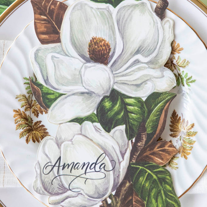 Close-up of an elegant place setting featuring a Magnolia Blooms Table Accent with "Amanda" written in beautiful script resting on the plate.