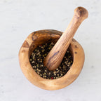 Wooden mortar and pestle with peppercorns on a light background.