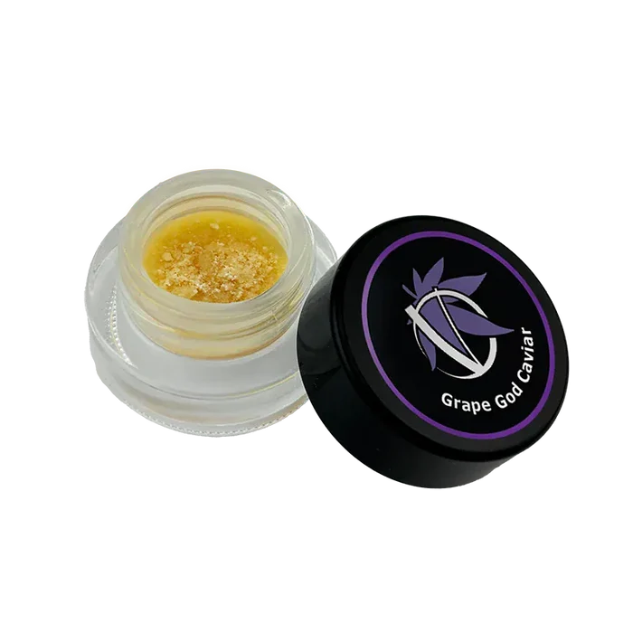Angled top view of an open jar showing golden crumble beside the black lid labeled Grape God Caviar.