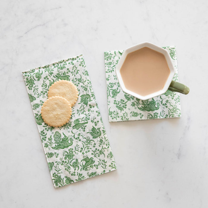 A cup of coffee and cookies on a white table adorned with Hester & Cook's Green Regal Peacock Napkins.