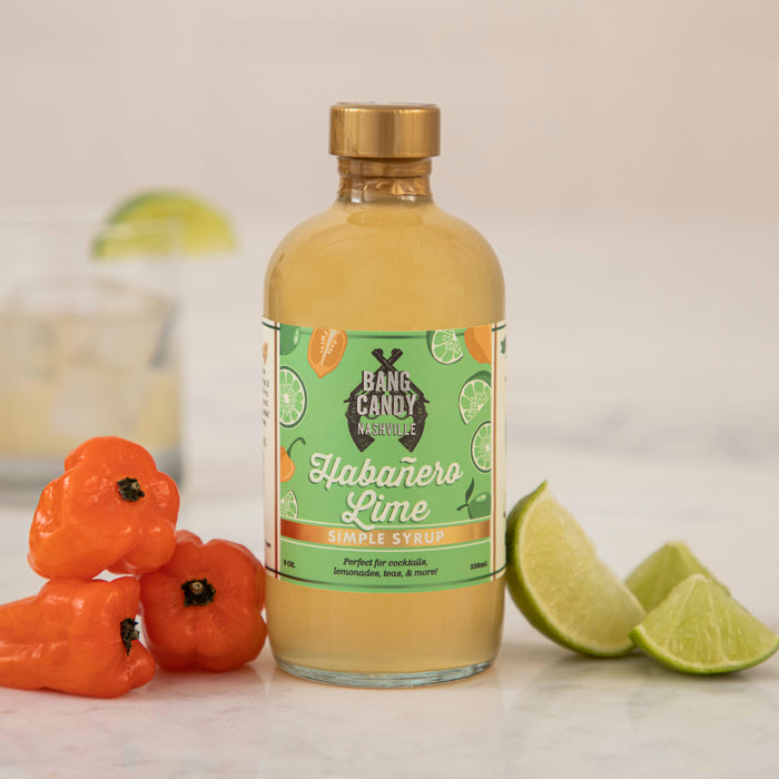A bottle of tequila with limes and Hester & Cook Habanero Lime Syrup next to it.