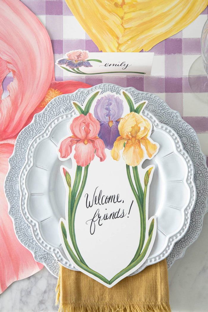 Top-down view of an elegant floral place setting featuring an Iris Table Card with "Welcome, friends!" written on it in beautiful script resting on the plate.