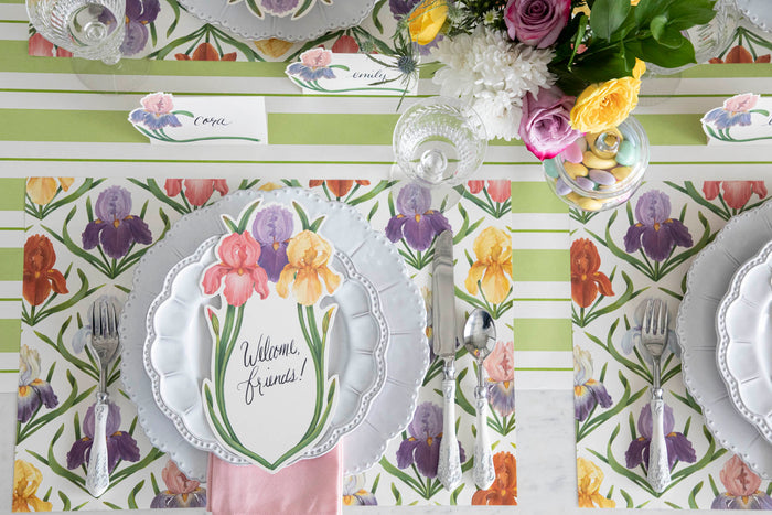 Top-down view of an elegant floral place setting featuring an Iris Table Card with "Welcome, friends!" written on it in beautiful script resting on the plate.