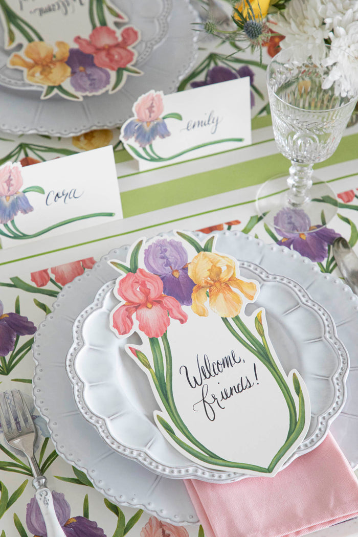 An elegant floral place setting featuring an Iris Table Card with "Welcome, friends!" written on it in beautiful script resting on the plate.