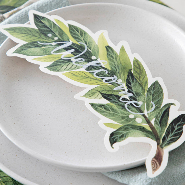 An elegant place setting featuring a Laurel Table Accent with "Welcome" written on it in white ink resting on the plate.