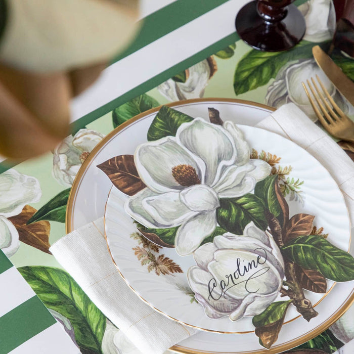 An elegant place setting featuring a Magnolia Blooms Table Accent with "Caroline" written in beautiful script resting on the plate.