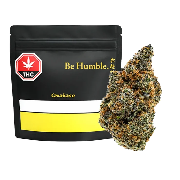 Front view of a black resealable bag labeled "Be Humble. Omakase" beside a close-up of a frosty green and orange bud.