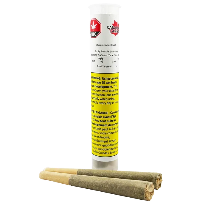 Tall front view of the Organic Apex Kush PR 2 x 1 g clear plastic tube with a yellow warning label, shown standing behind three pre-rolled joints.