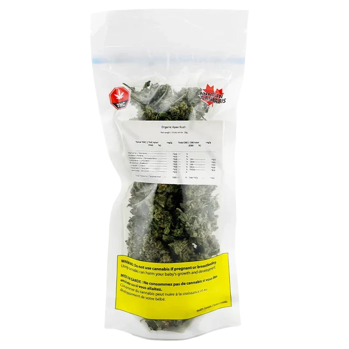 Clear front-facing view of a sealed bag of Organic Apex Kush showing dense green buds, a white label of contents, and a yellow warning panel.