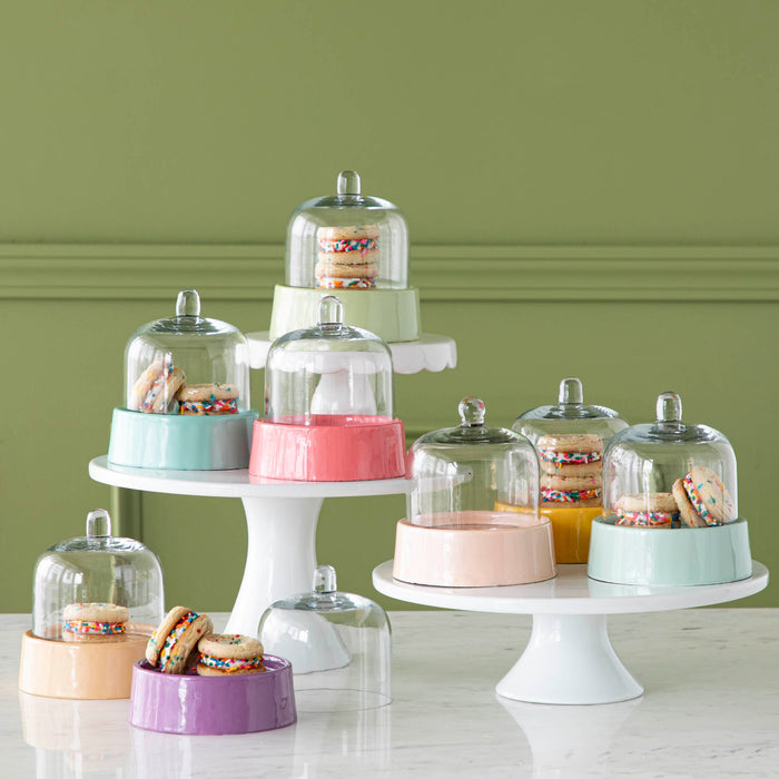 A collection of Petite Sweet Cake Domes in various pastel colors, some sitting atop white cake stands and some containing treats inside.