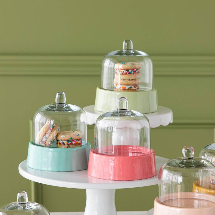 A teal, mint, and hot pink Petite Sweet Cake Dome atop two white cake stands with treats inside.