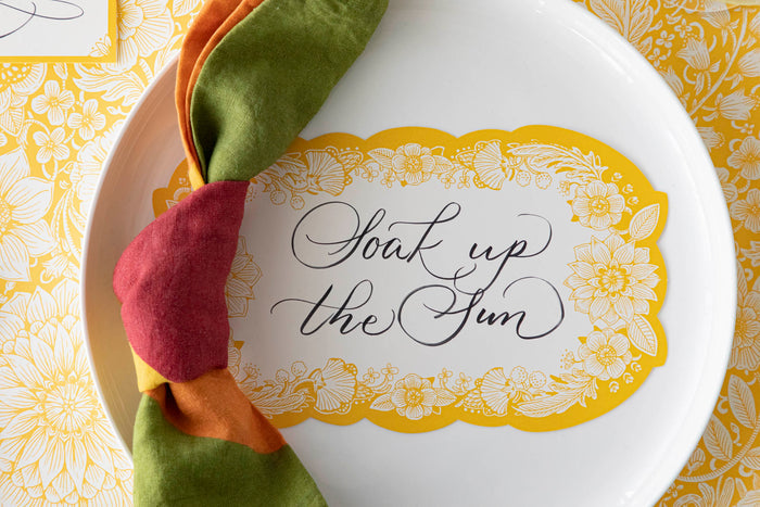 Close-up of a Spring Blooms Table Card with "Soak up the sun" written on it in lovely script resting on the plate of a vibrant place setting.